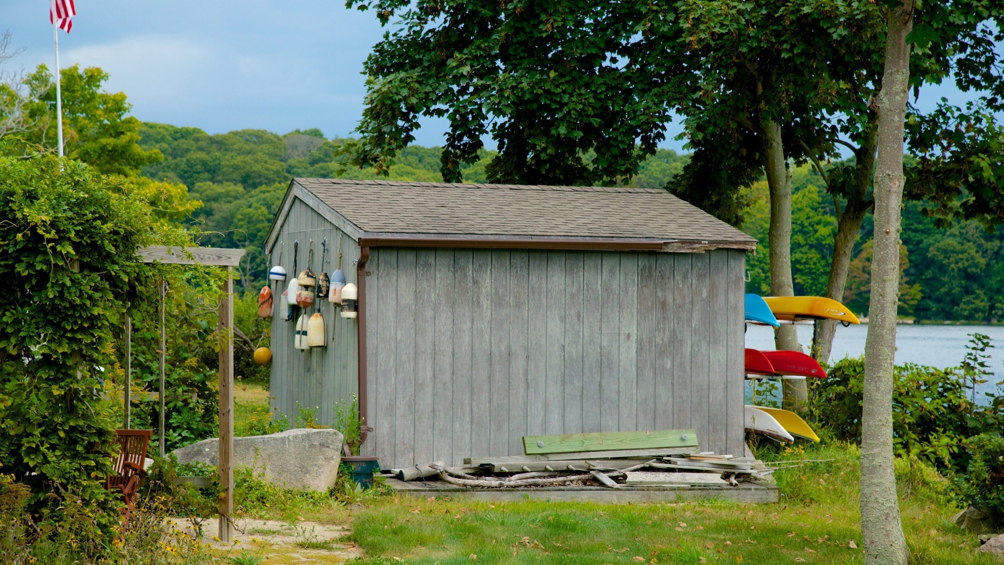 A wooden shed by a lake with a flag, boats, and greenery.
