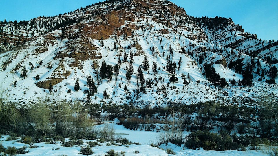 A snow-covered mountain with a rocky peak and dense forest.