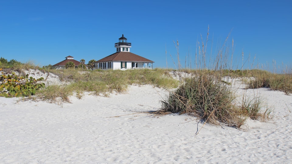 A lighthouse on a sandy beach with sparse vegetation.