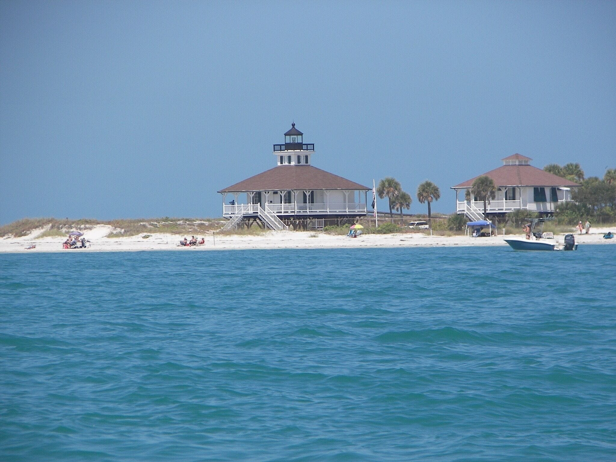 A beach with two white houses, a boat, and people on the sand.