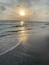 Een strand met golven, een steiger en de zon die ondergaat.