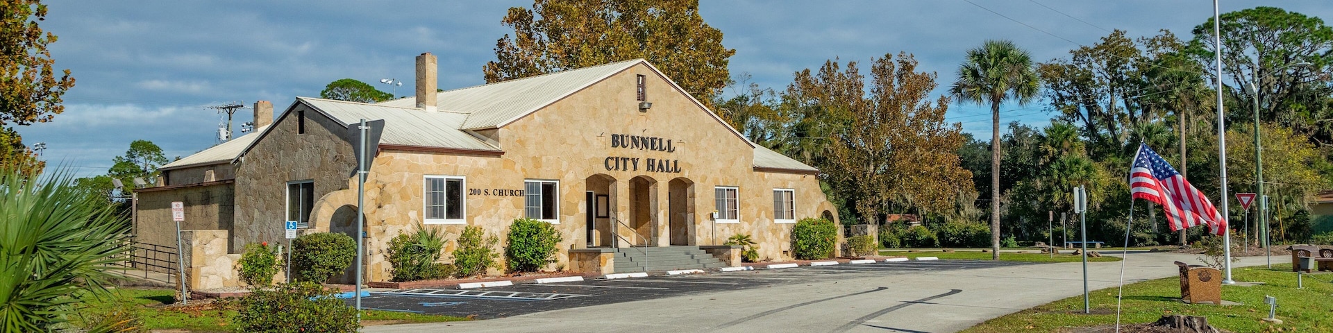 El Ayuntamiento de Bunnell, con fachada de piedra, un asta con la bandera estadounidense y una calle al frente.