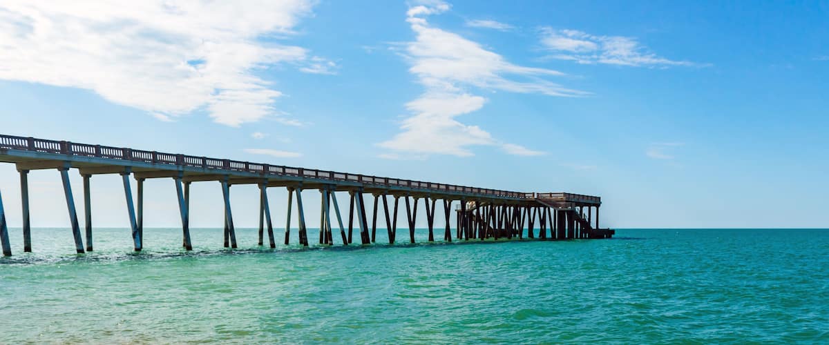 A long pier extending into a turquoise sea under a clear sky.