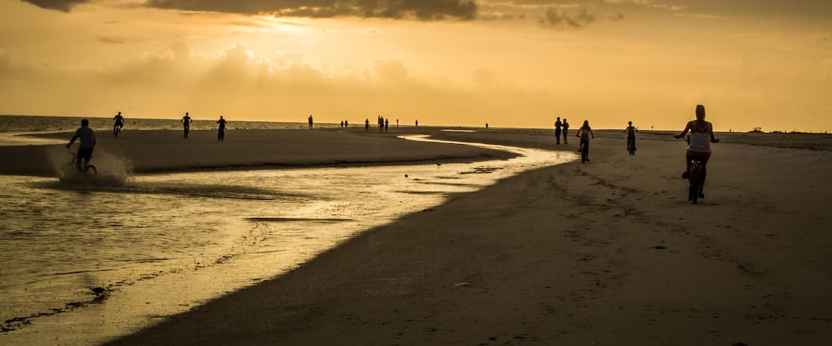 A beach at sunset with people walking and riding bicycles.