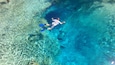 Una persona nadando en aguas azul cristalina, con rocas y formaciones de coral visibles bajo el agua.