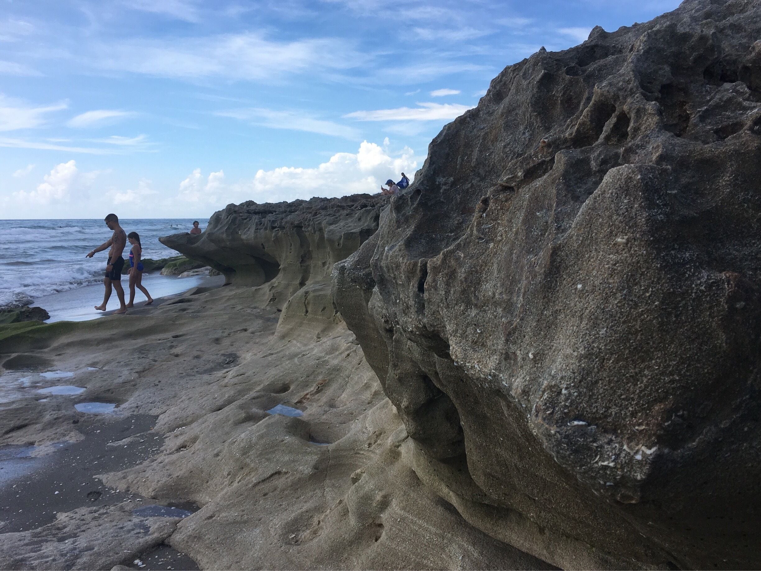 A rocky coastline with two people walking along the shore.