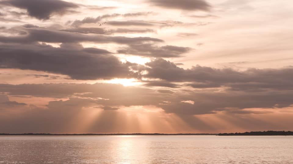 A sunset over a calm body of water with clouds and a distant shoreline.