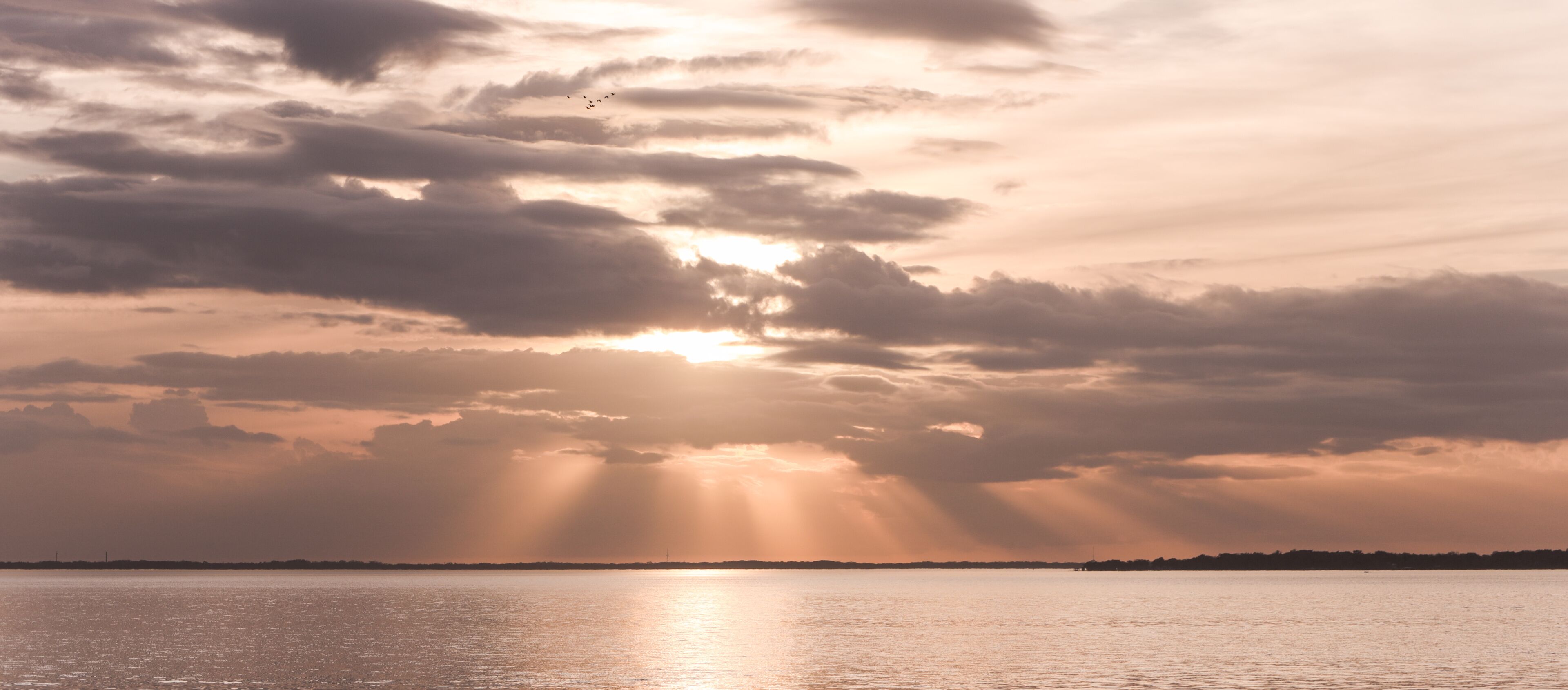 A sunset over a calm body of water with clouds and a distant shoreline.