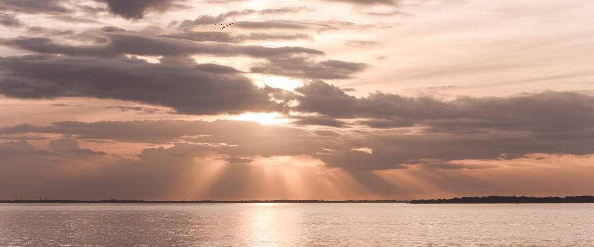 A sunset over a calm body of water with clouds and a distant shoreline.
