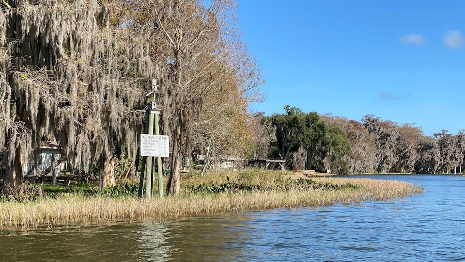 A calm lake with trees covered in Spanish moss, a signpost, and a wooden dock.