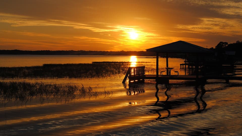 A sunset over a body of water with a dock and a gazebo.