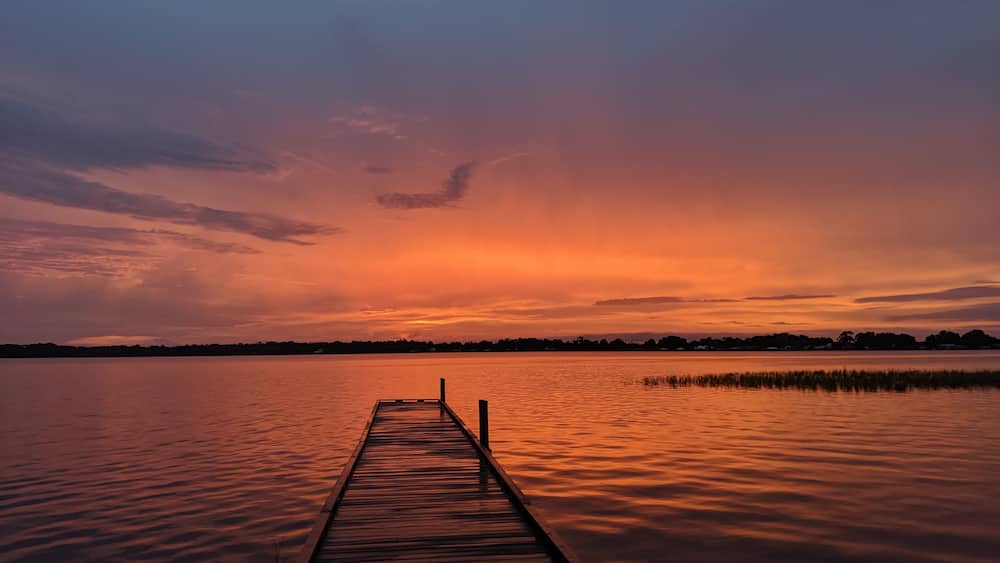 Eine hölzerne Mole, die sich in einen ruhigen See bis zum Sonnenuntergang erstreckt.