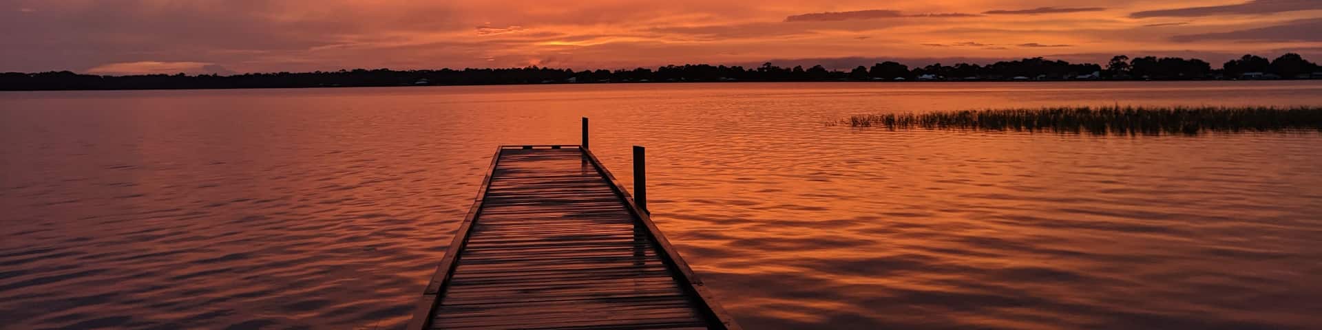 A wooden pier extending into a calm lake during sunset.