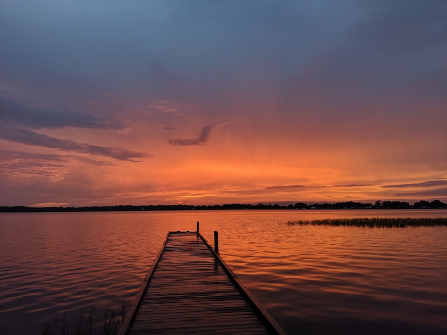 A wooden pier extending into a calm lake during sunset.