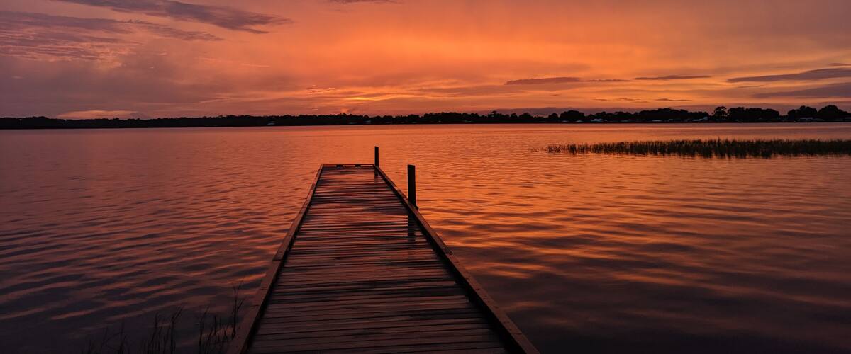 A wooden pier extending into a calm lake during sunset.