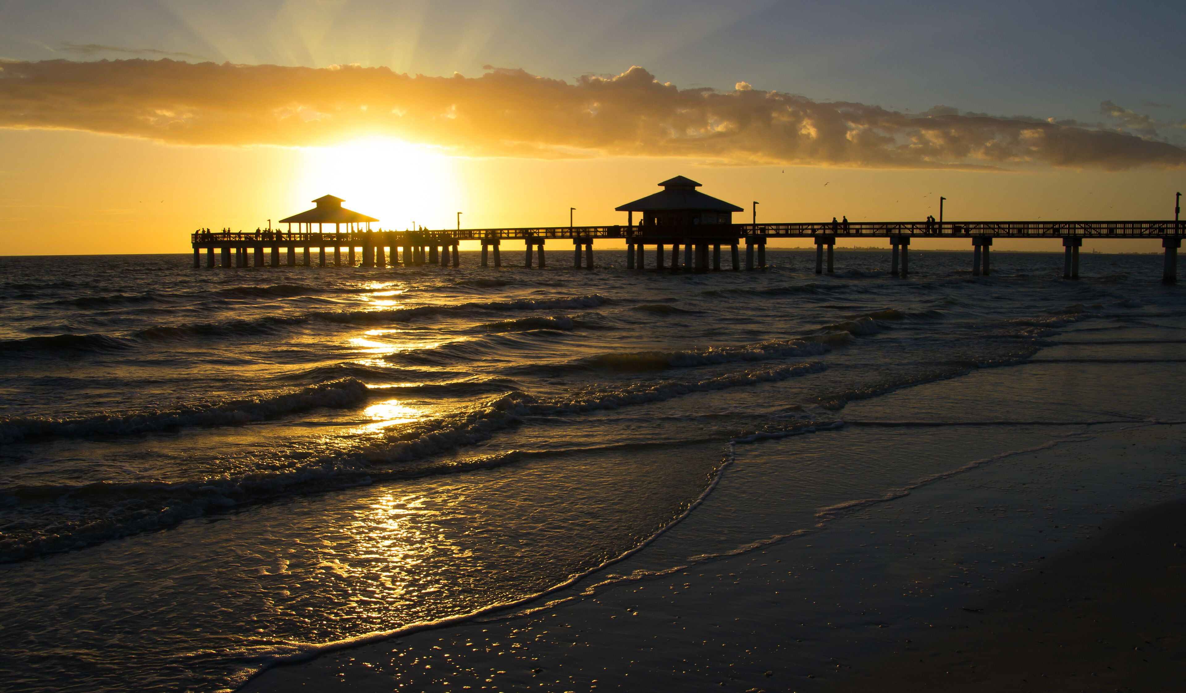 A pier extending into the ocean at sunset with waves lapping at the shore.