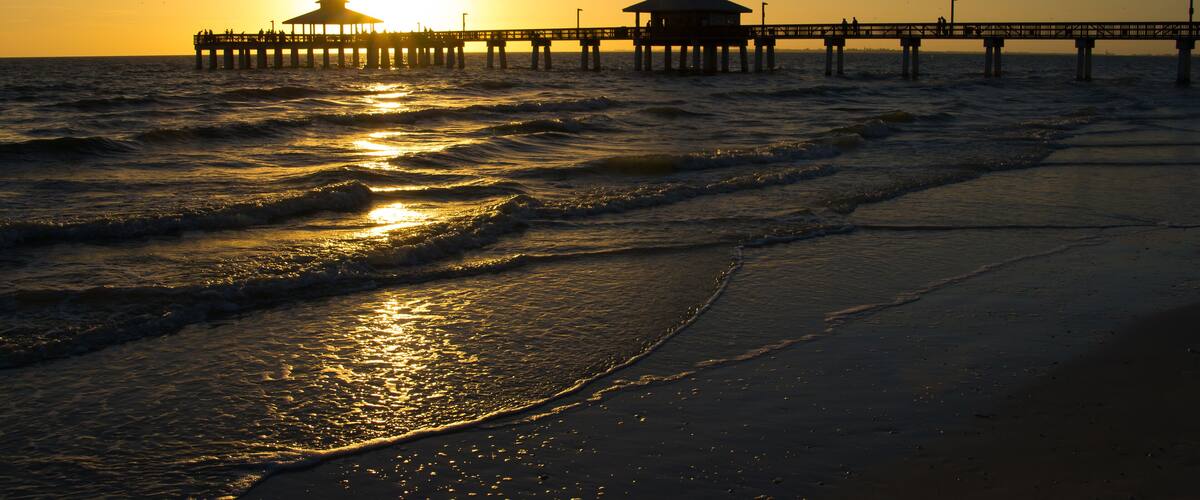 A pier extending into the ocean at sunset with waves lapping at the shore.