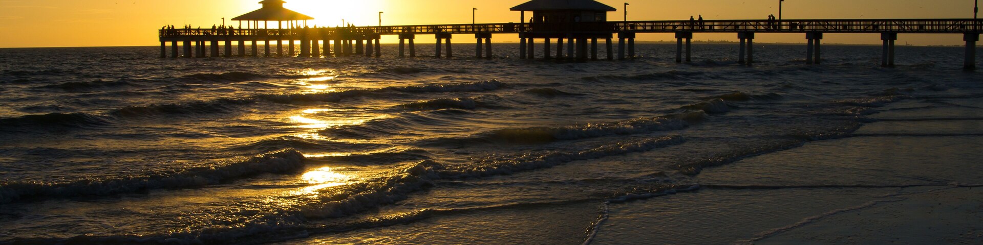 A pier extending into the ocean at sunset with waves lapping at the shore.
