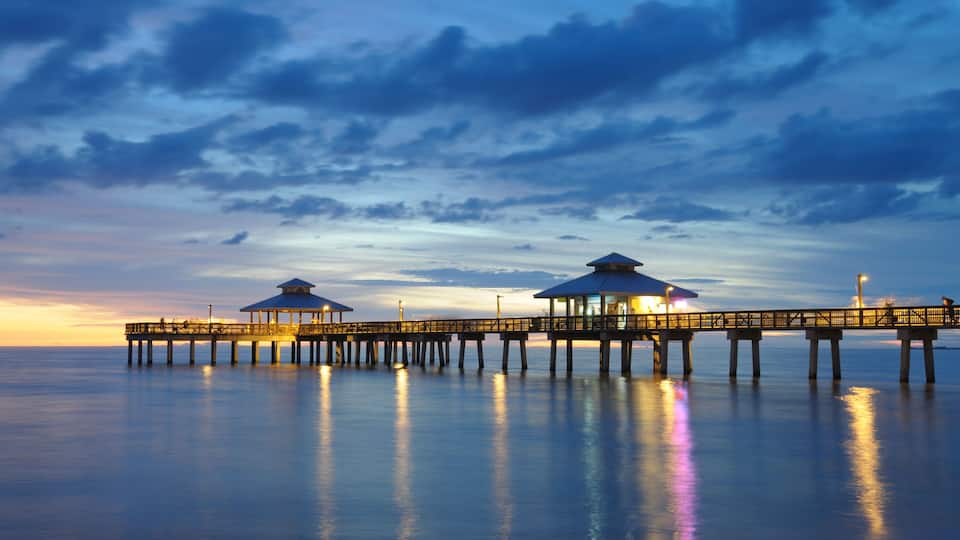A pier with two gazebos extending into calm waters at sunset.