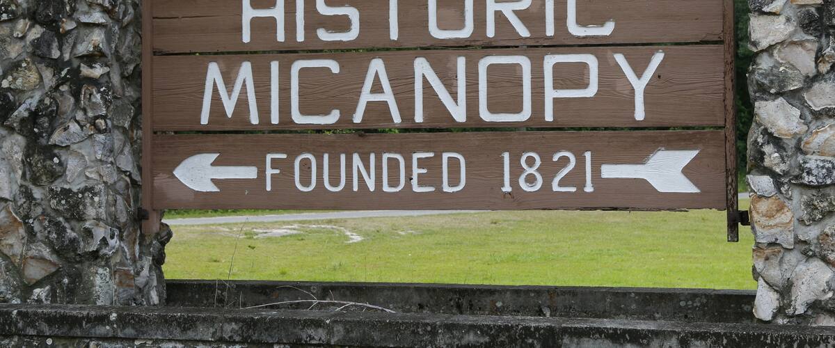 A wooden sign with the text "HISTORIC MICAANY Founded 1821" and arrows pointing left and right.