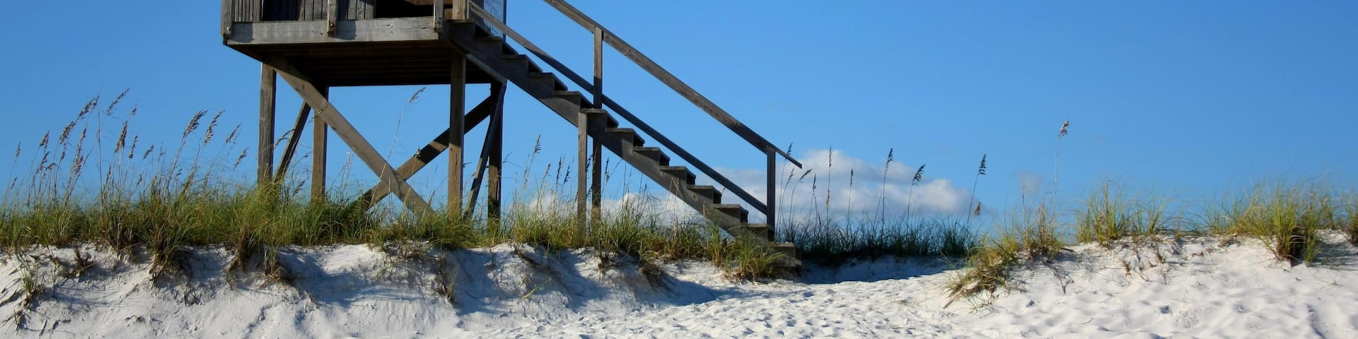A wooden lifeguard tower on a sandy beach with a clear blue sky.