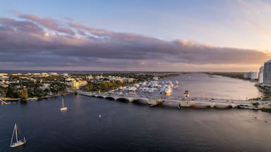 A marina with boats, a bridge, and a cityscape with buildings and a sunset.