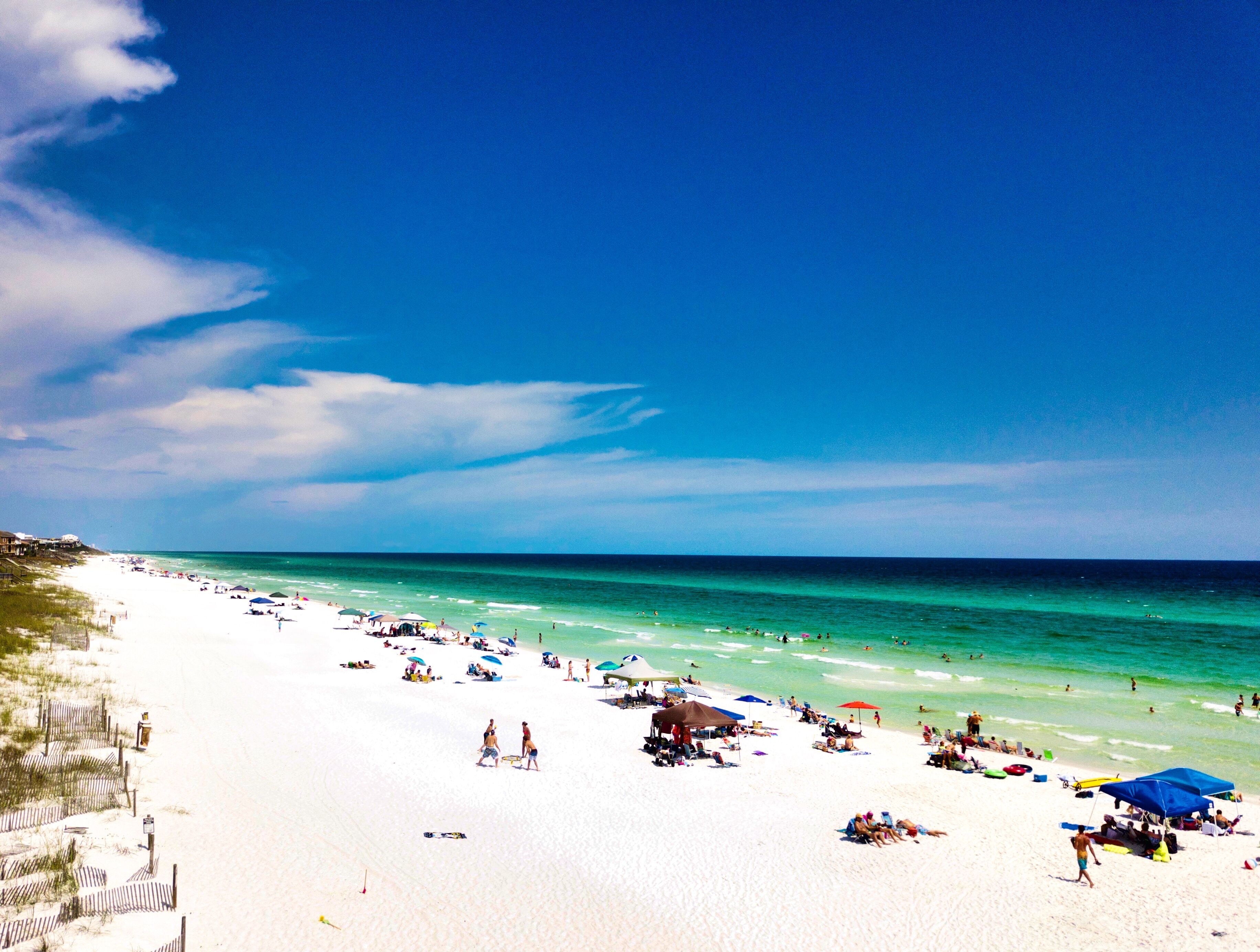 A beach with white sand, clear turquoise water, and a few people sunbathing.