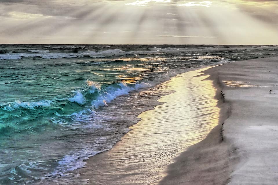 A beach with waves crashing onto the shore and the sun setting in the background.