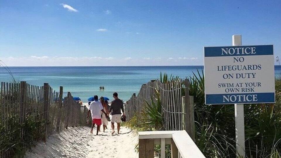 Ein Strand mit einem Schild, das darauf hinweist, dass keine Rettungsschwimmer im Dienst sind und zum Schwimmen auf eigene Gefahr auffordert.