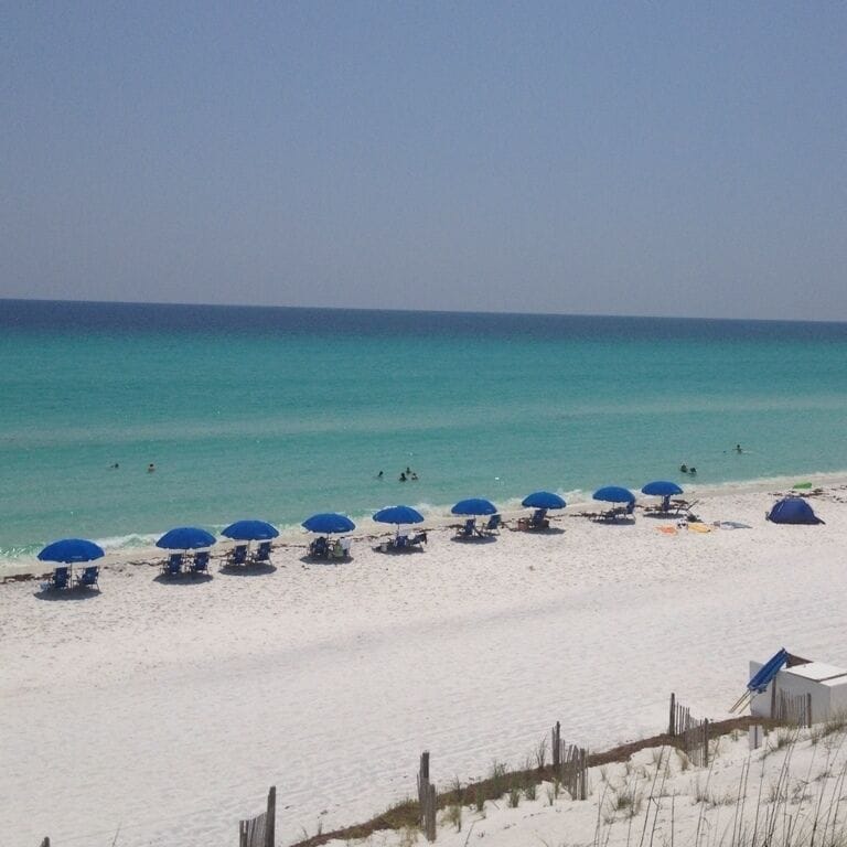 A beach with white sand, turquoise water, and blue umbrellas.