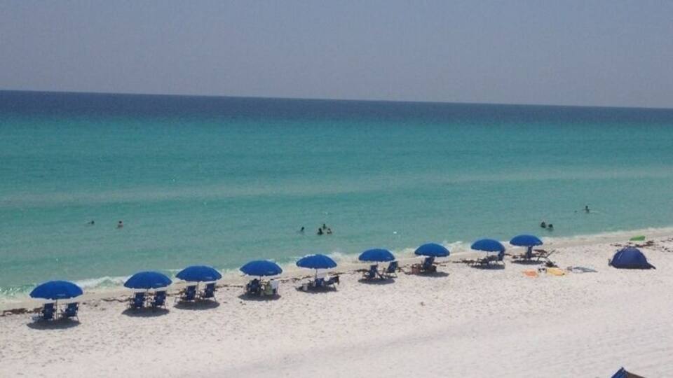 A beach with white sand, turquoise water, and blue umbrellas.