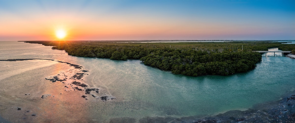 A sunset over a coastal landscape with a small island surrounded by water.