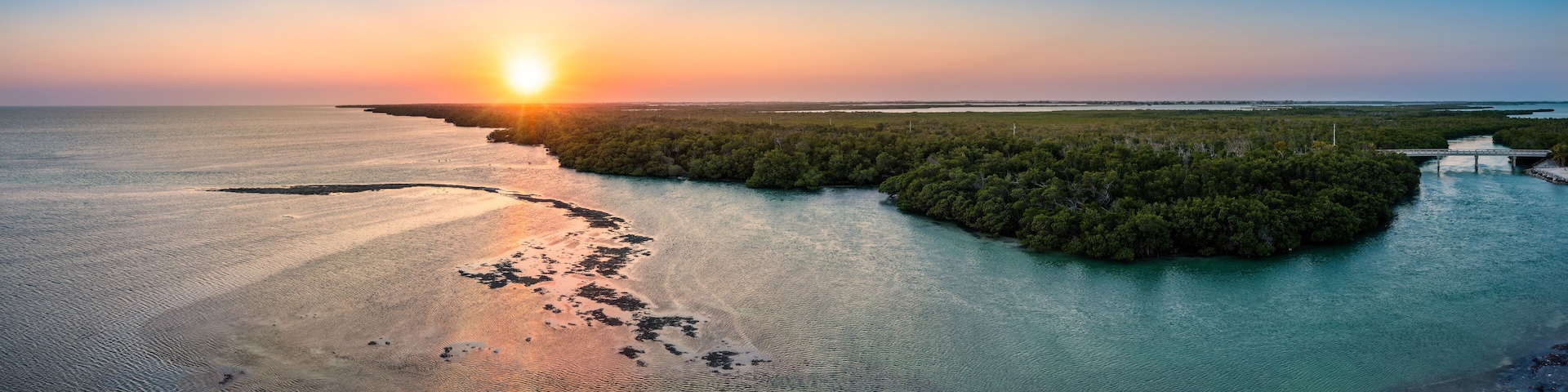A sunset over a coastal landscape with a small island surrounded by water.
