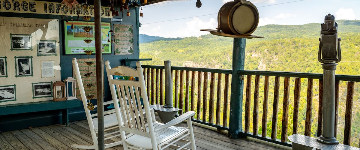 A wooden deck with a white rocking chair, a metal lantern, and a signboard with information about the Gorge Information.