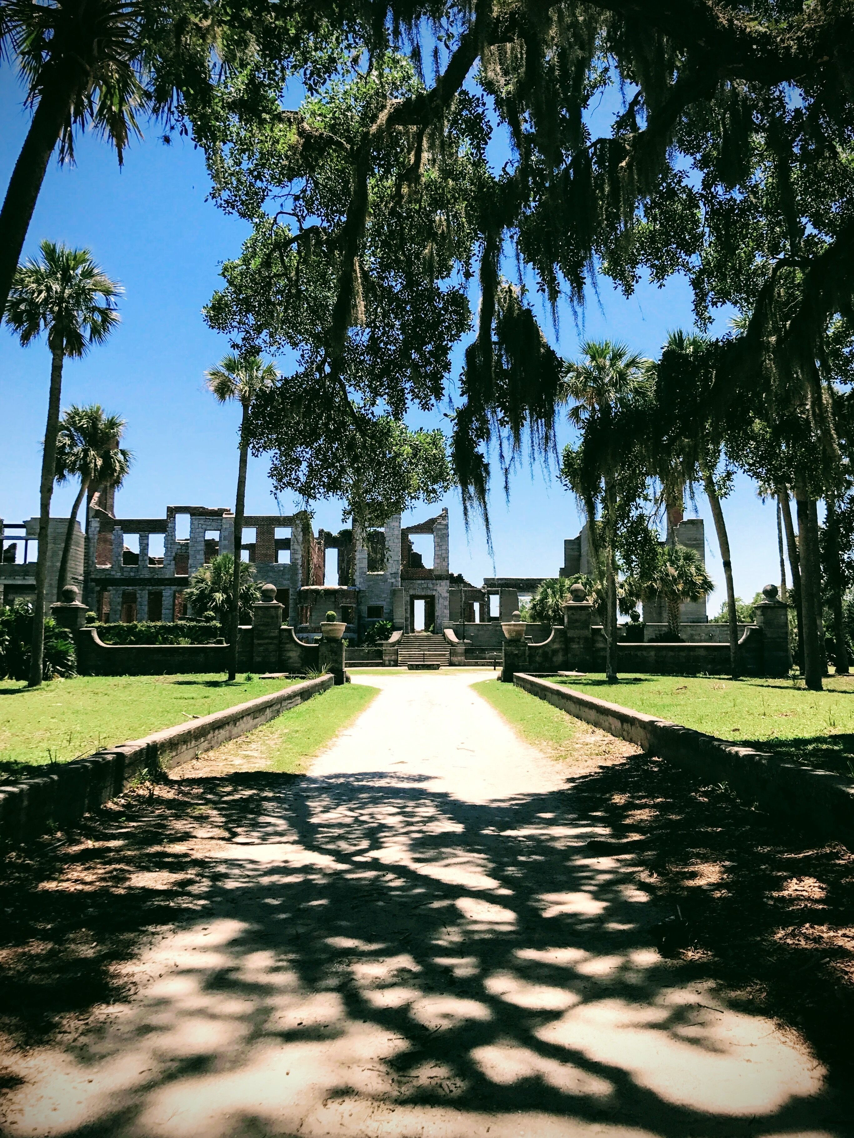 A pathway leading to a historic building with stone walls and palm trees.