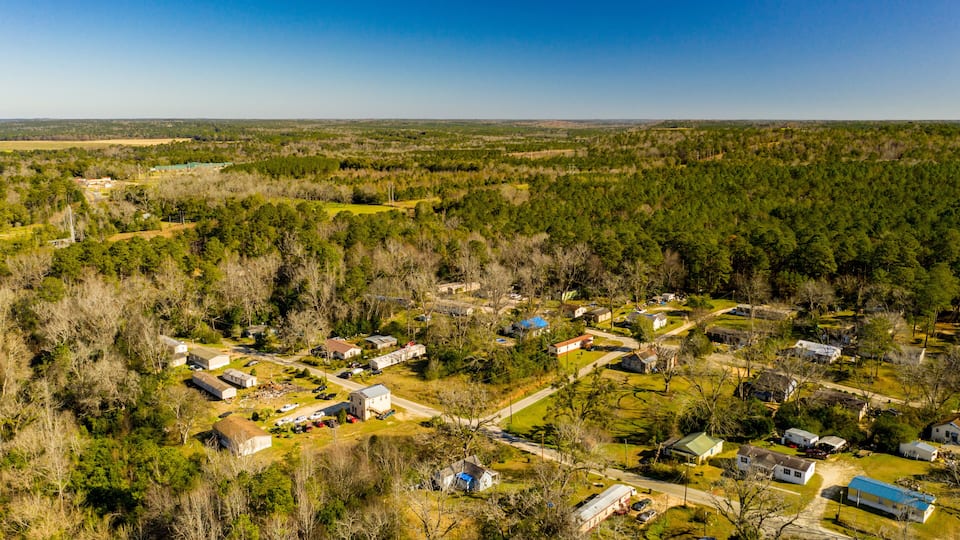 An aerial view of a small rural community surrounded by dense forests and open fields.