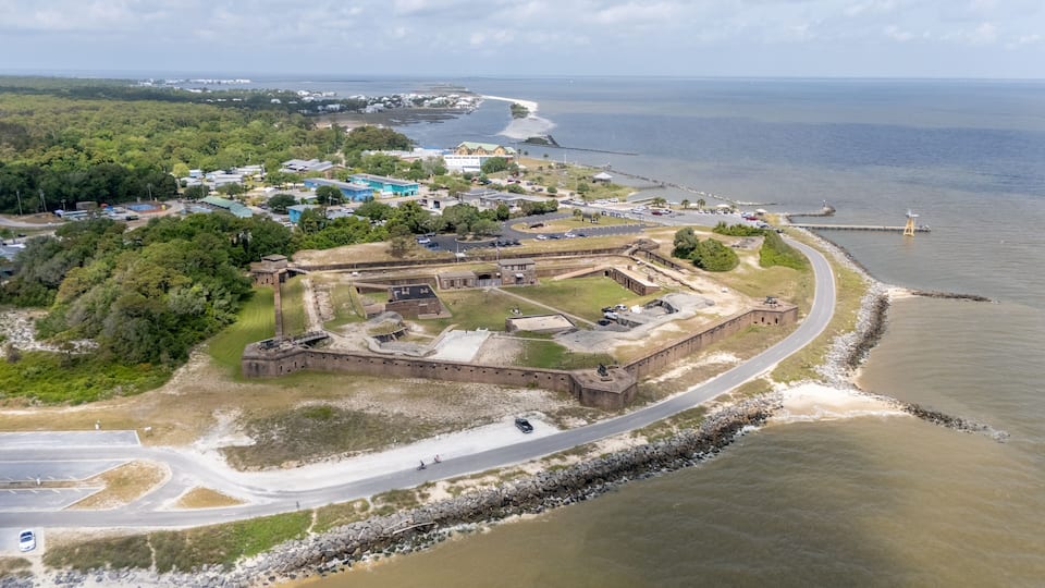 An aerial view of a coastal fortification with surrounding buildings and a bridge in the background.
