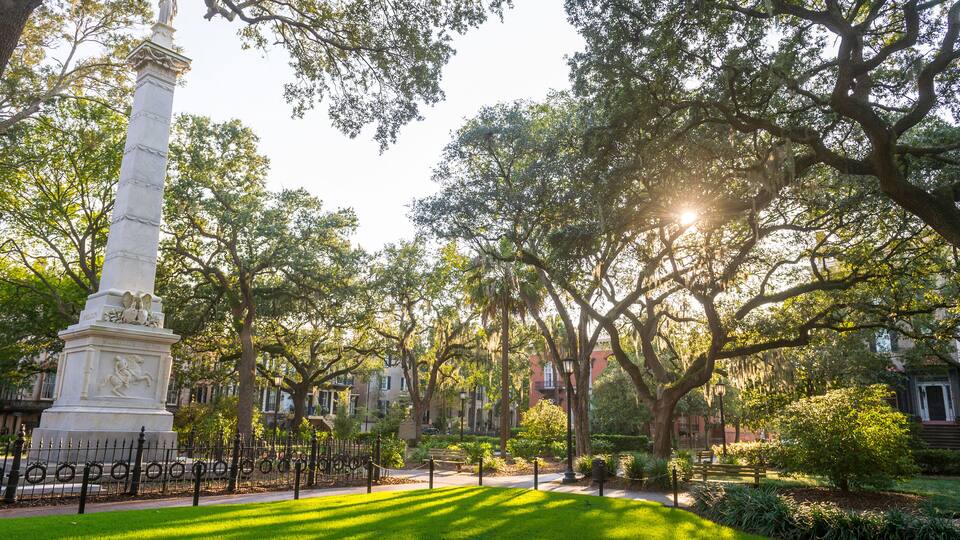 A park with a white monument, lush green grass, and mature trees.