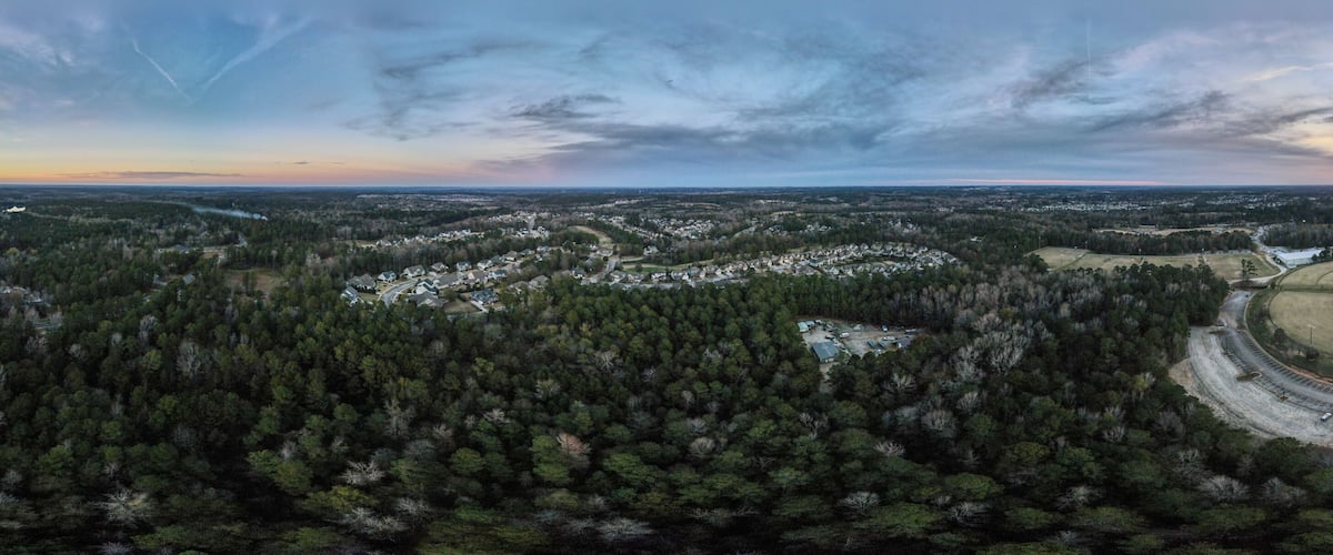 A rural landscape with dense forests, a baseball field, and a winding road.
