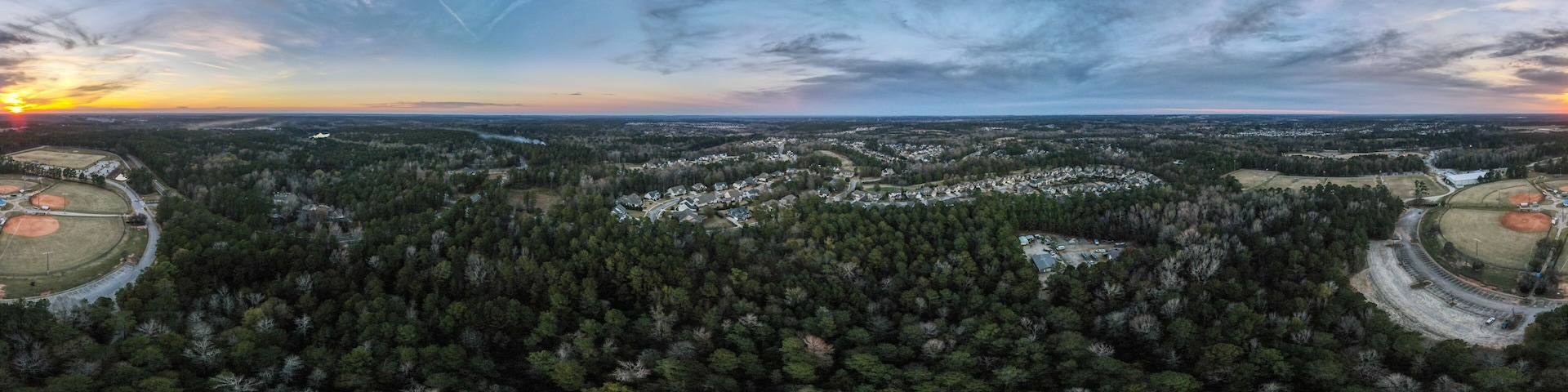 A rural landscape with dense forests, a baseball field, and a winding road.