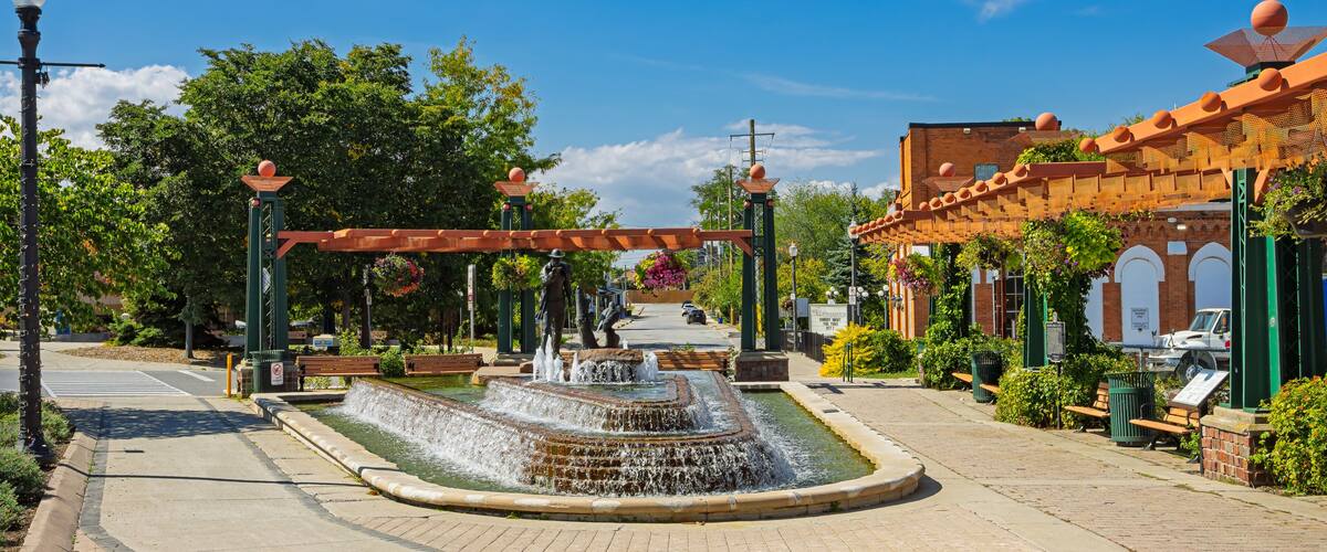 A fountain, a pedestrian walkway, and a building with a red roof.