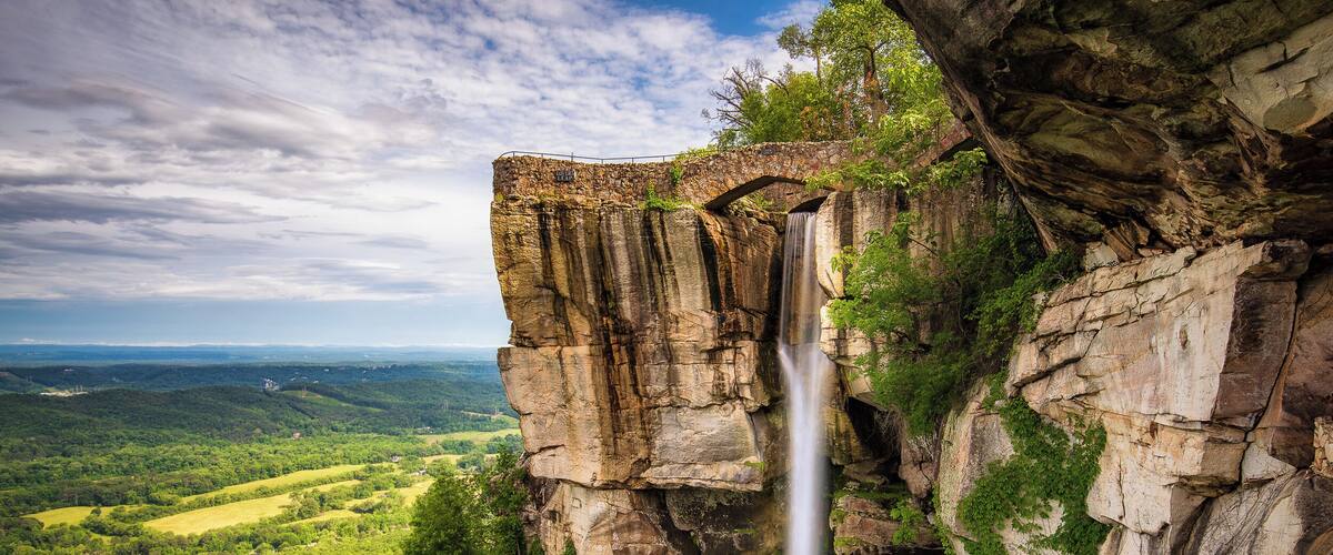 A waterfall cascading down a rocky cliff surrounded by lush greenery.
