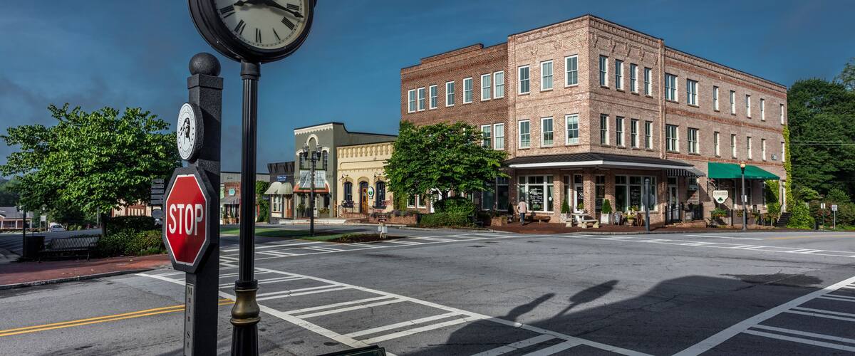 A street corner with a stop sign, a clock, and a sign for a pizza restaurant.