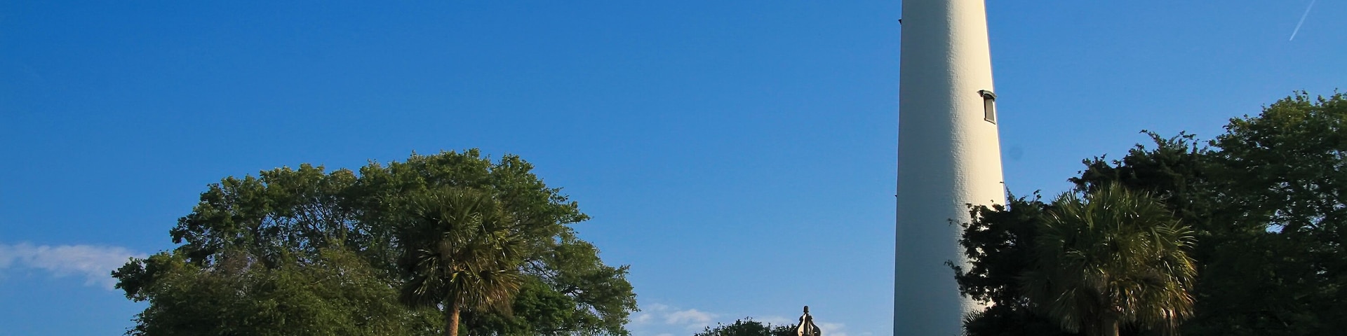 Un faro, una escalera de madera y un pabellón rodeado de árboles y rocas.