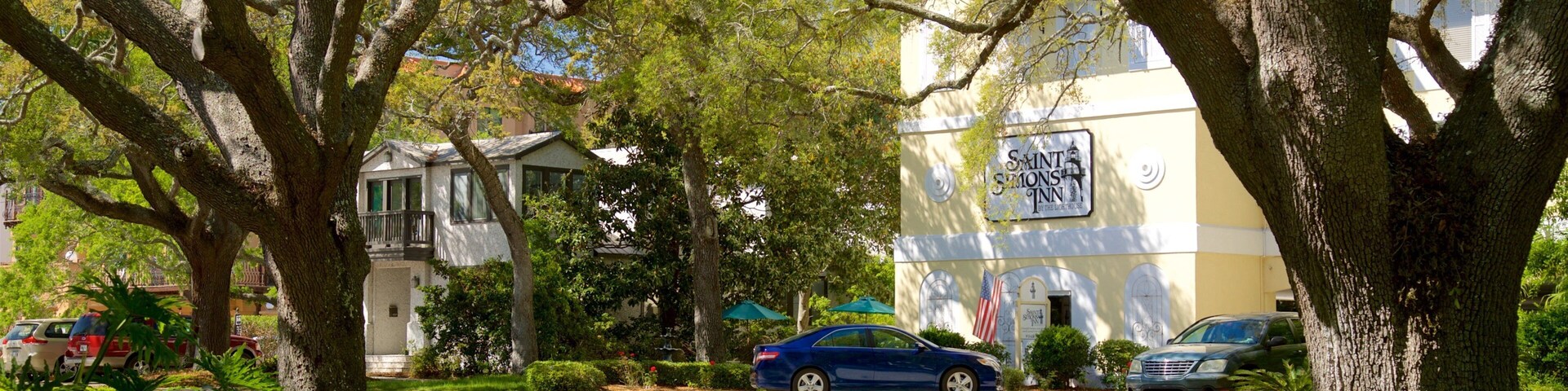 Una calle bordeada de árboles y con coches aparcados, con un edificio en el fondo que dice 'Saints Monks Inn'.
