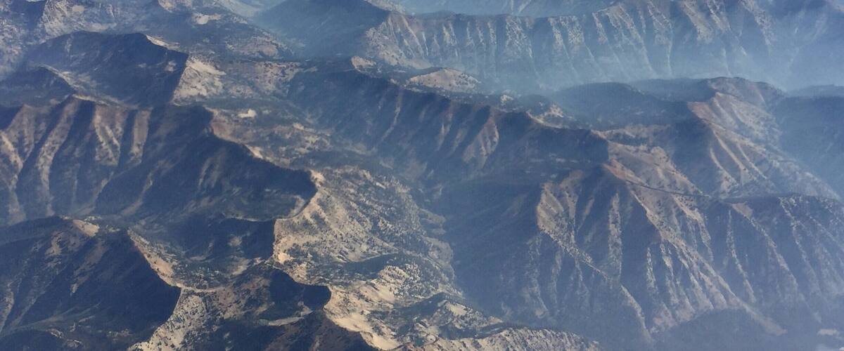 A mountainous landscape with layered peaks and valleys, partially obscured by mist or low clouds.