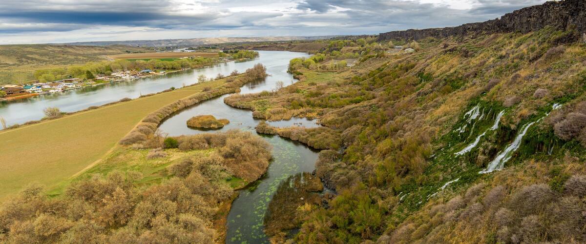 A river winding through a valley with a small town on the left and a waterfall on the right.