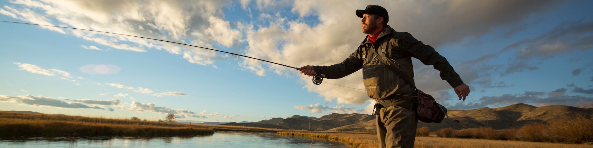 A person fishing by a calm lake with a mountainous backdrop.