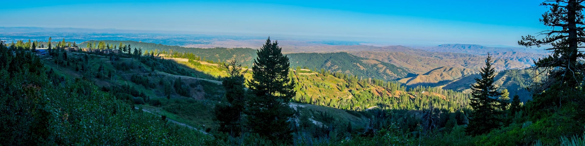 A mountainous landscape with dense forests, a clear blue sky, and distant hills.