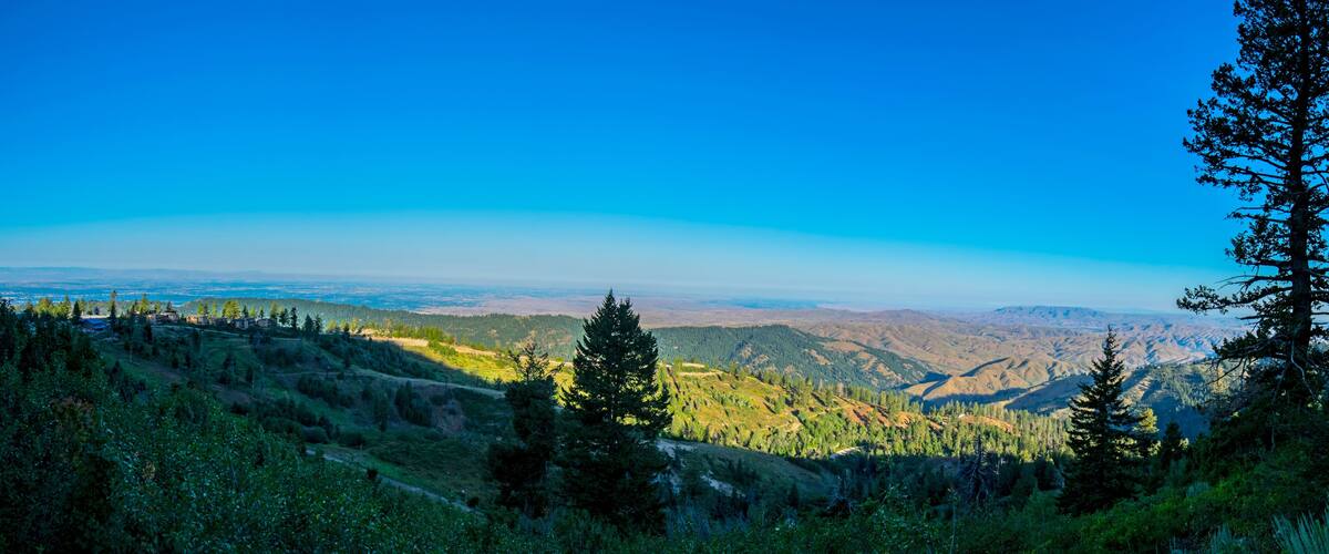A mountainous landscape with dense forests, a clear blue sky, and distant hills.